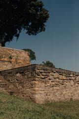 Obraz premium Old masonry wall. Stone wall style walls of a huge farm with old house, trees, blue flowers and grazing horses.