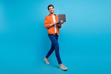 Full size profile portrait of positive nice man hold wireless netbook walking isolated on blue color background
