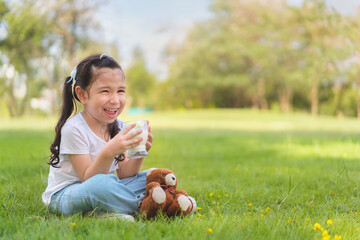 Caucasian mix girl drinking milk from glass sitting on grass at outdoor park, Whiskers from milk,...