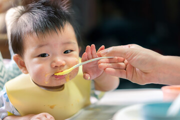 Asian baby girl with apron eat food by spoon and mother feed her, Healthy nutrition of solid food...