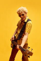 Smiling, artistic, expressive young man with curly blonde hair, in sunglasses playing guitar...