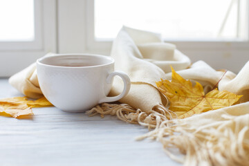 autumn leaves with a cup of tea or coffee next to a scarf on a wooden background with copy space