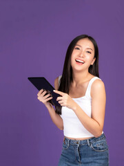 Beautiful Asian brunette woman cute girl in white tank top playing a smart phone , tablet computer isolated on purple background - mobile phone uses a online banking for pay online shopping