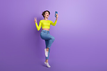 Fototapeta na wymiar Full size photo of excited pretty girl hold smart phone make selfie show v-sign empty space isolated on violet color background
