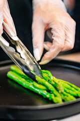 woman chef hand put green asparagus on plate