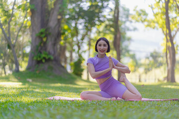 Asian woman doing yoga posing on mat in outdoor park Young healthy woman yoga exercise, yoga pose in natural environment for body, mind, health. Relax concept.