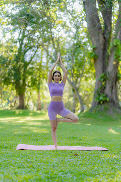 Healthy Thai Asian woman doing yoga in the evening at the park. Health and outdoor activities concept with plants as background on green grass. vertical image