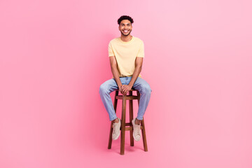 Full length photo of young applicant man wear t-shirt denim jeans sitting bartender chair waiting his turn isolated on pink background