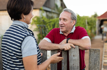Two gardeners friendly talking outdoors next to wooden fence of country estate on day