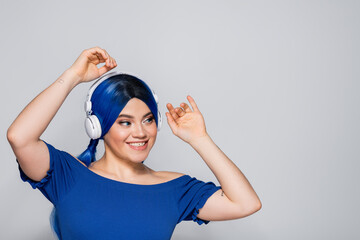 self expression, positive young woman with blue hair listening music in wireless headphones on grey background, vibrant youth, individualism, modern subculture, tattoo, sound