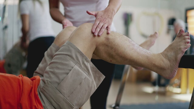 Physical therapist helping senior man to use Pilates machine, old age workout routine, body wellness and stength