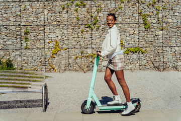 Full body length shot of african female student driving motorized kick scooters in the city ,...