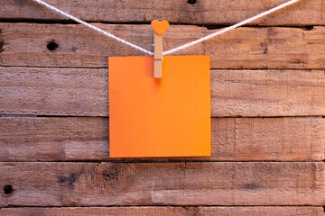 Orange paper note hanging on a thread on wooden background