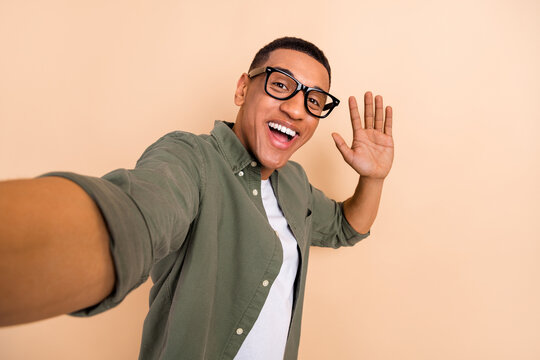 Portrait of cheerful positive nice man wear stylish shirt eyewear making selfie waving arm to you isolated on beige color background