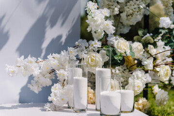 Candles. Decor details closeup. Location for luxury wedding ceremony. Arch decorated white flowers, greens, greenery. Trendy decor in backyard. Celebration baptism concept. Birthday party reception.