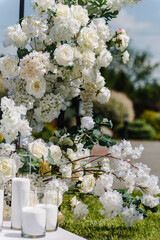 Decor details closeup. Location for luxury wedding ceremony. Arch decorated white flowers, greens, greenery, candles. Trendy decor in backyard. Celebration baptism concept. Birthday party reception.