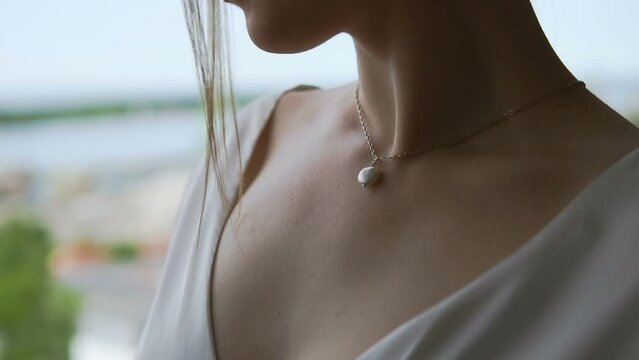A young woman is standing near the window. Jewelry on the neck of the bride. A pendant given by a beloved man. Beautiful neck. Dress with a deep neckline.