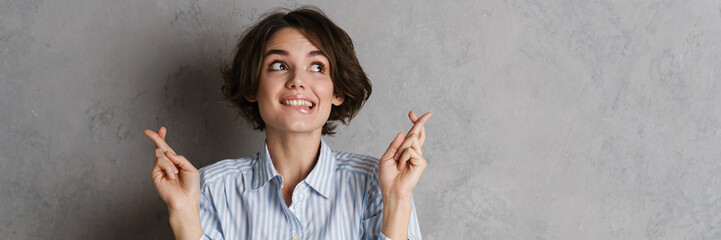 Young brunette woman holding fingers crossed for good luck
