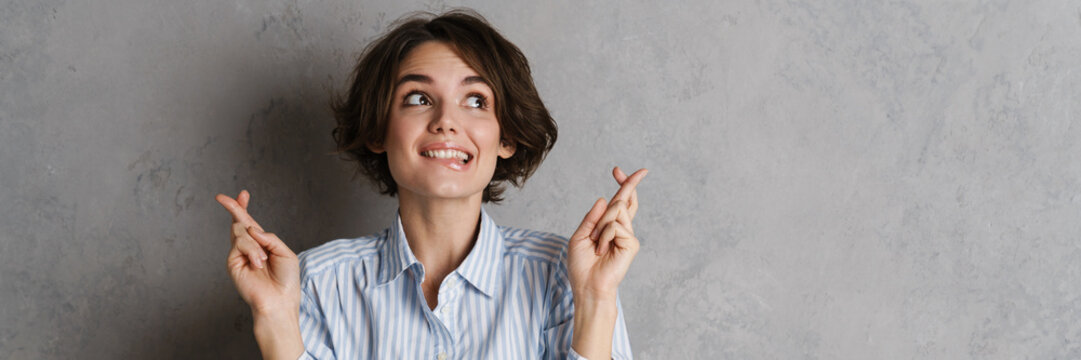 Young brunette woman holding fingers crossed for good luck