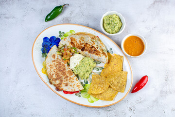 Mexican shredded chicken quesadilla, flour tortilla, refried beans, pico de gallo, accompanied by guacamole and nachos on a beautiful handcrafted painted plate