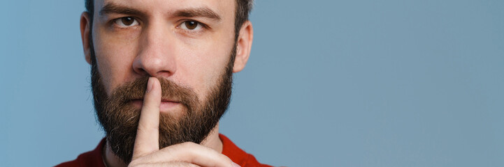 Brunette white man with beard smiling and showing silence gesture