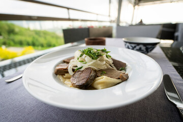 Composition of tasty Kazakh national dish beshbarmak in a plate with kazy, flour tortillas, onion on a table in a restaurant