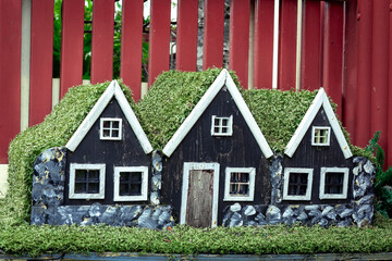Three small black wooden elf houses with green moss roof, typical for Iceland. 