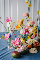 Fototapeta na wymiar Summer composition of garden flowers. Festive decorated with flowers, fruits, greenery, candles. Bouquet in vase, orange, pomelo, grapefruit on table. Home interior with decor spring elements.