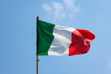 Italian tricolor flag waving with a clear sky in the background.
