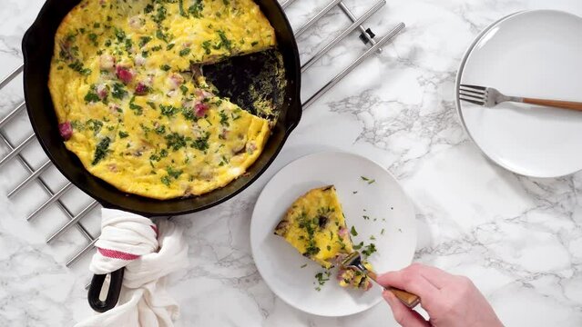 Flat lay. Slicing freshly baked spinach and ham frittata in cast iron skillet.