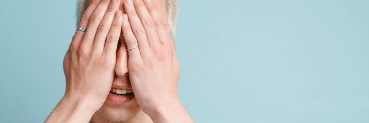 Young blonde man in shirt smiling and covering his eyes