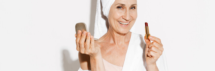 Senior woman wearing towel smiling while applying lipstick