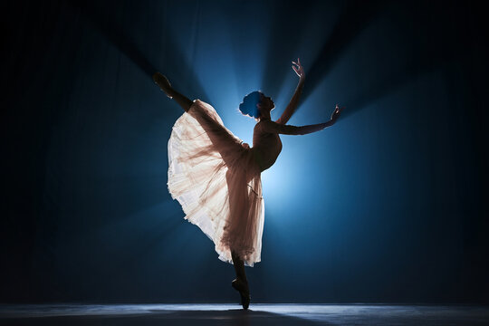 Elegant, tender, slim, talented girl, female ballet dancing dancing against dark blue background with spotlight