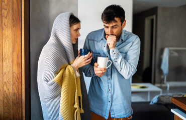 Freezing couple covered with a blanket. Man and a woman wrapped in a warm blanket in a cold room.