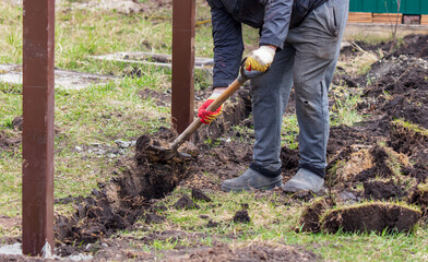 A worker digs the ground with a shovel to install a fence