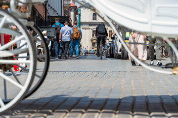 A cyclist and a group of young men on the cobbled street of the old city past cars behind a white horse-drawn carriage in the foreground, sustainable development and authenticity. Travel destinations