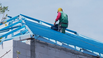 Workers are installing gray roof tiles wearing seat belts to ensure safe working at heights.