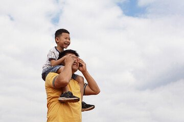 The son rides on his neck and covers his father's eyes with his hands while exercising together at the stadium. Outdoor activities concept with family, father and son.  