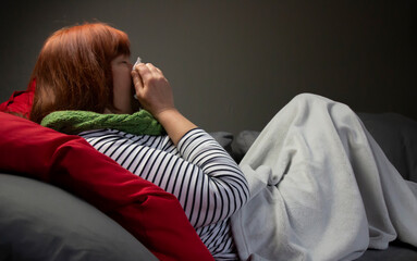 Frau schneutzt / putzt sich die Nase - Frau liegt unter einer Decke auf dem Sofa und ist erk&auml;ltet
