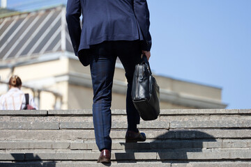 Man in a business suit with leather briefcase climbing stone stairs in city, male legs in motion on...