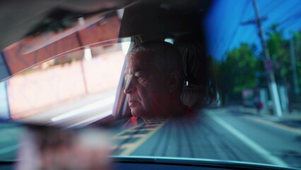 Older man driving car seen through rearview mirror on city road. Senior driver behind steering wheel