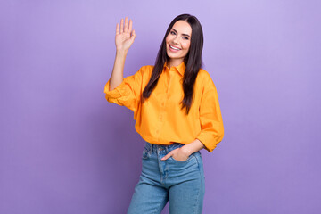 Photo of positive cheerful friendly business woman wear orange shirt denim jeans waves palm greetings isolated on violet color background © deagreez