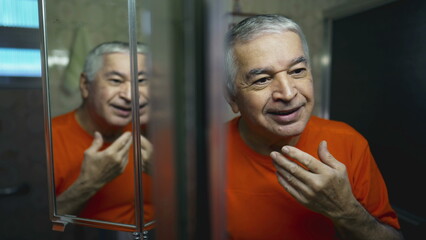 Happy senior man looking at himself in mirror reflection. Joyful emotion of elderly person laughing and smiling in morning ritual