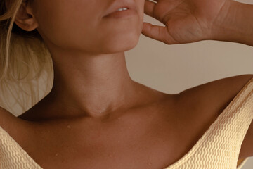 Cropped shot of young blonde tanned woman with sweat drops on her chest lifting her hair on beige...