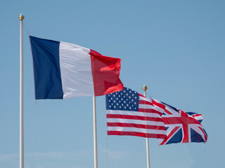 The flags of France, USA and the European Union (EU) waving in the wind on a flagpoles with blue sky background.