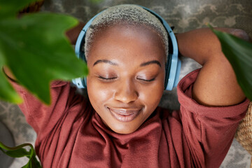 Woman, face and headphones for listening to music to relax on a floor with plants for peace and...