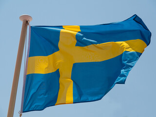 Sweden the Swedish flag waving in the wind on a flagpole with blue sky background.