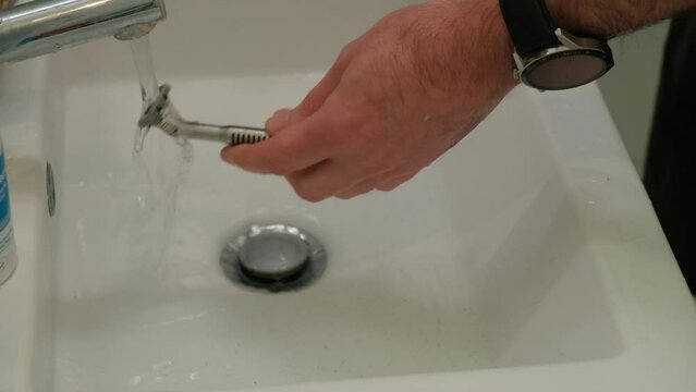 Cleaning shaving razor in bathroom sink. Rinsing off razor with water.