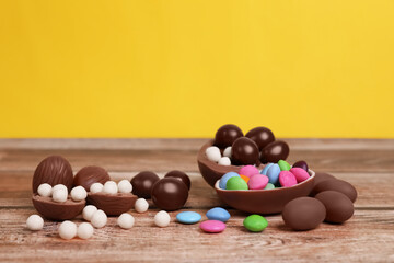 Delicious chocolate eggs and candies on wooden table against yellow background
