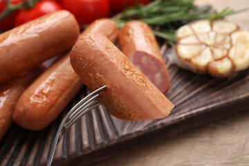 Delicious vegan sausage on fork over wooden table, closeup